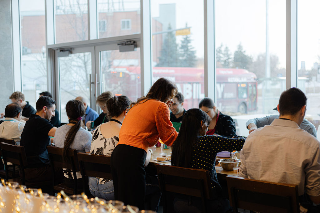 A corporate group cooking together at long tables during a team-building class at the YW Calgary Community Kitchen in Inglewood, Calgary