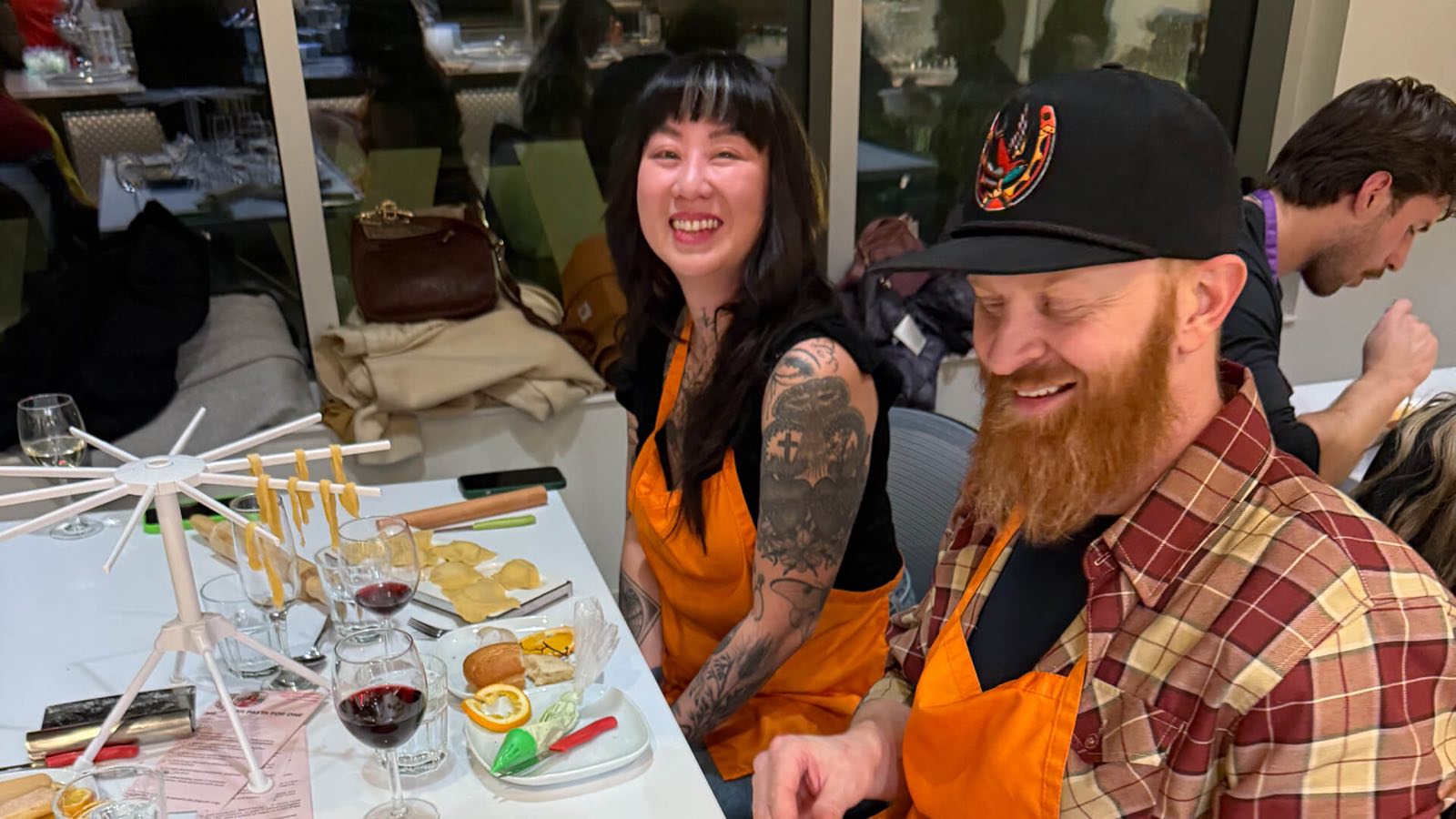 A couple in aprons laughing over the fresh pasta and red wine they made together at Stirring It Up in Calgary