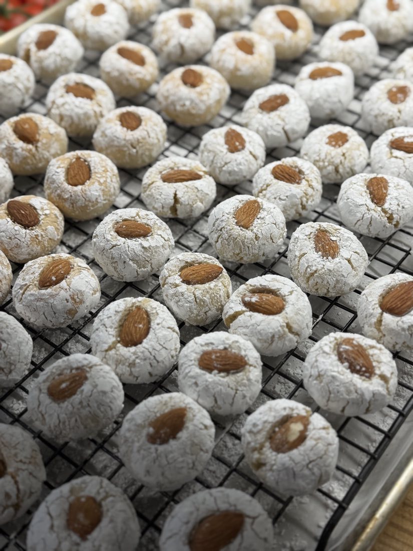 Trays of Italian almond cookies dusted with icing sugar, each topped with a whole almond