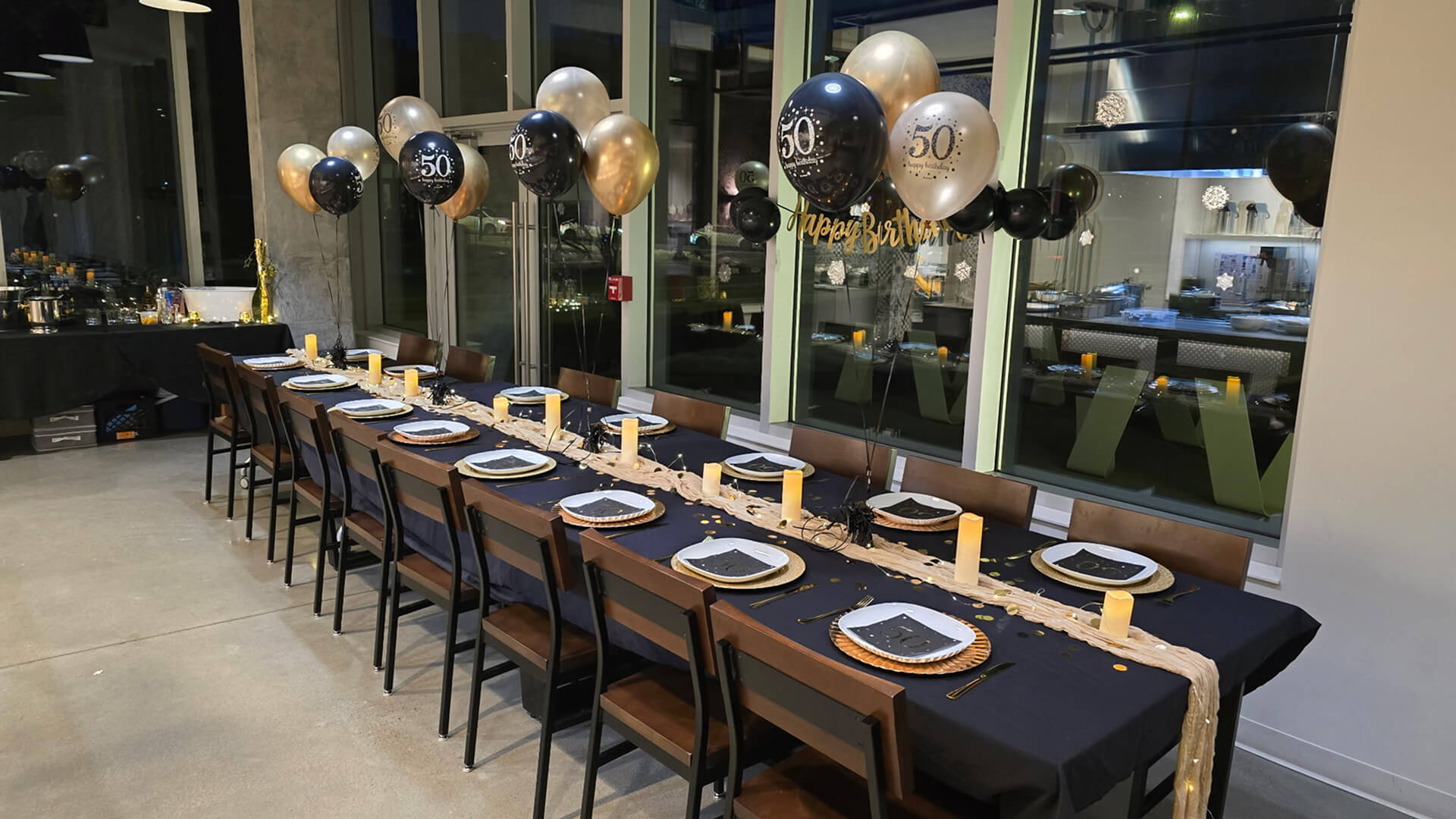 A private event space set with black-and-gold balloons, candles, and elegant place settings for a birthday celebration at Stirring It Up in Calgary